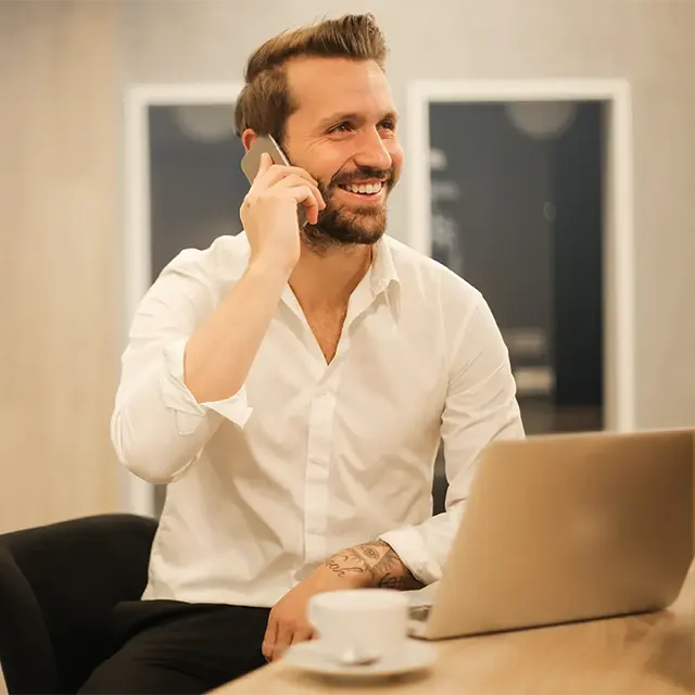 Hombre de negocios hablando por teléfono celular y trabajando en un computador portátil.